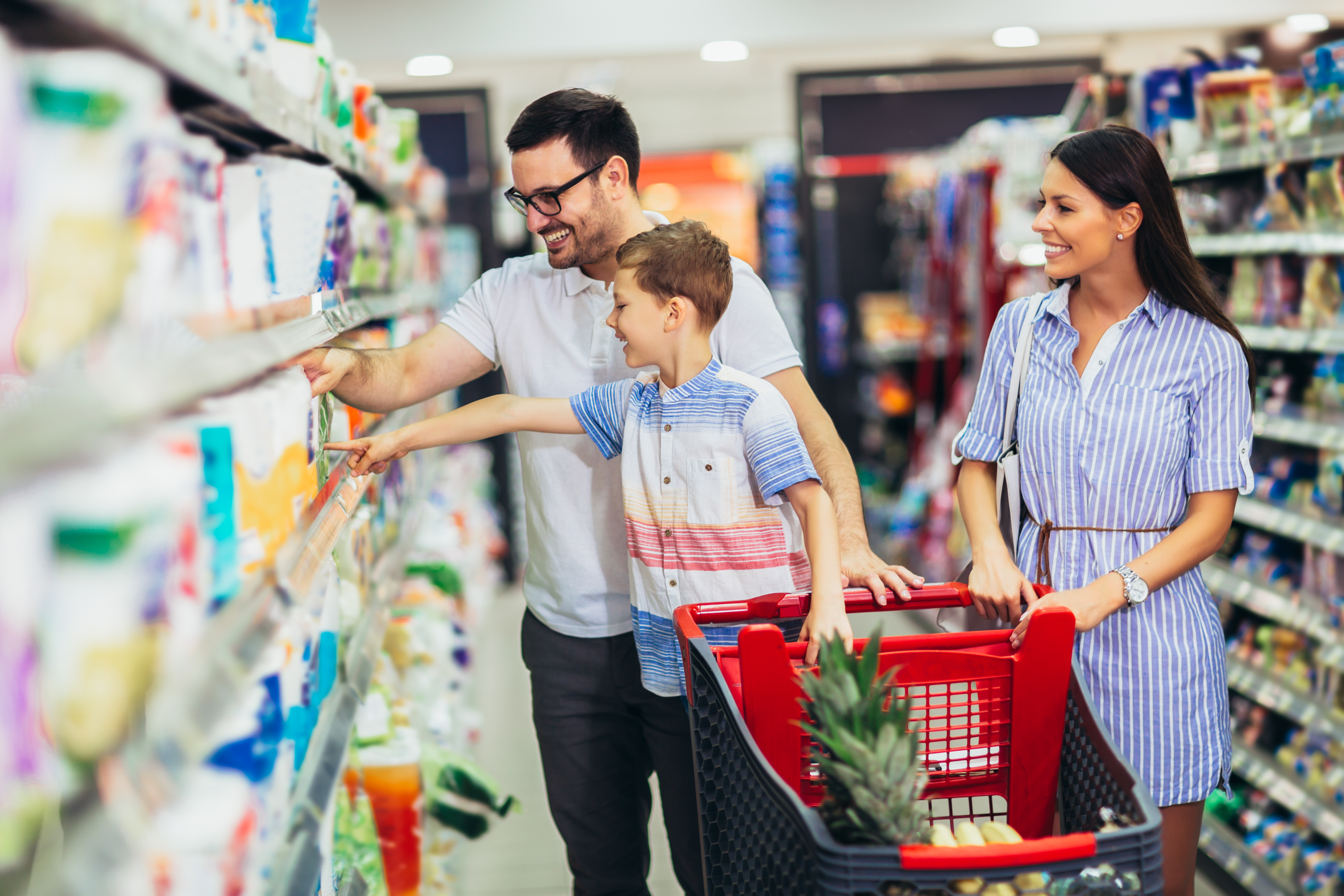 Happy family with child and shopping cart buying food at grocery store or supermarket